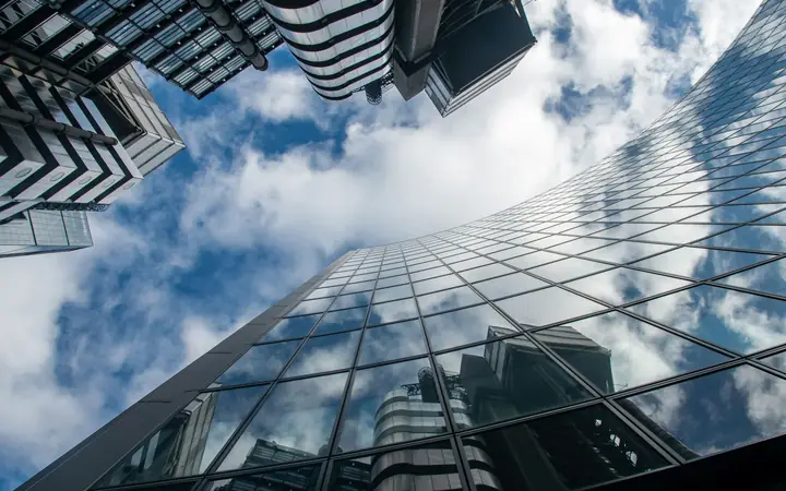 Edificio de vidrio visto desde abajo con nubes reflejadas