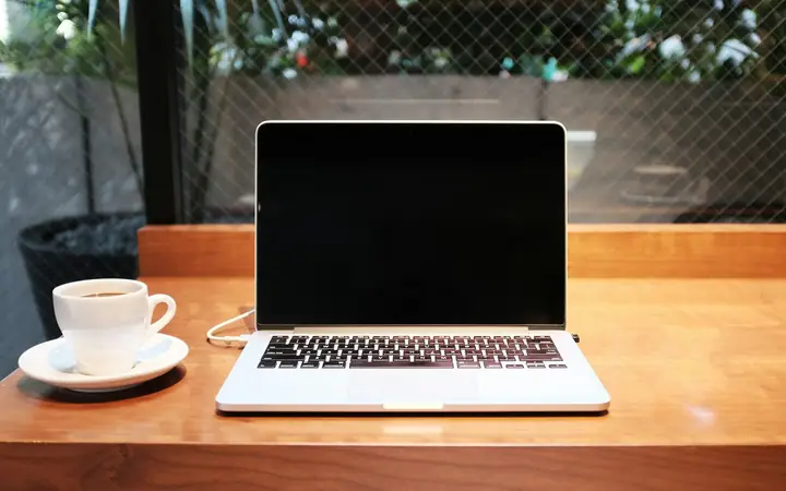 Computador portátil y una taza de café sobre una mesa de madera
